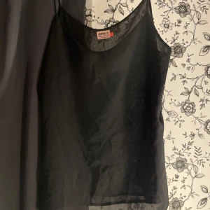 Svart ärmlös topp från ONLY - Säljer en snygg svart ärmlös topp från ONLY. Den är gjord av ett lätt och luftigt material, perfekt för varma dagar eller som ett lager under en jacka. Toppen har en enkel och stilren design som passar till många olika outfits.