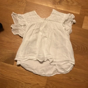 Vit blus från Gina Tricot - Säljer en söt vit blus från Gina Tricot i storlek 146/152. Blusen har korta ärmar med volangdetaljer och en v-ringad hals. Perfekt för sommarens varma dagar eller en fin fest. Materialet känns lätt och luftigt, vilket gör den bekväm att bära.