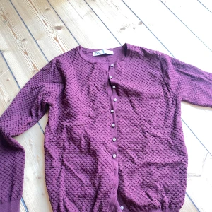 Lila stickad kofta från Zara - Säljer en superfin lila stickad kofta från Zara. Den har ett snyggt texturerat mönster och knäpps med glittriga knappar framtill. Perfekt för höst och vinter när du vill vara både varm och stilren. Koftan är i storlek M och är i mycket bra skick. Passar perfekt till både vardag och fest!