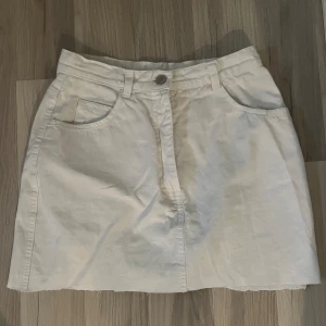 Vit kjol från Sinclair by Kappahl - Säljer en snygg vit kjol från Sinclair by Kappahl i storlek 36 (S). Kjolen är kort och har en klassisk design med två framfickor och en knapp i midjan. Perfekt för sommaren eller våren! 🥰