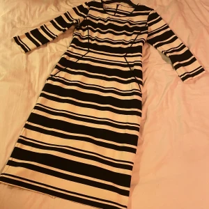 Randig klänning från Part Two - Säljer en superfin randig klänning från Part Two i storlek S. Klänningen är svart och vit med ett snyggt randigt mönster. Den är tillverkad av 66% viskos, 30% polyamid och 4% elastan, vilket gör den både bekväm och stretchig. Klänningen har trekvartsärmar och en normal passform. Perfekt för både vardag och fest!