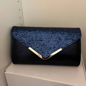 Marinblå kuvertväska - Säljer en superfin marinblå kuvertväska med glitter & silverdetaljer, perfekt som bal eller festväska. Finns en längre axelbandskedja inuti. Aldrig använd, 50kr + frakt💙