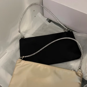 Festväskor i satin - Säljer 2st superfina festväskor i satin, en beige & en svart med superfint strass axelband. Enklare dustbag fås med till båda. Aldrig använda, 100kr + frakt för båda🤎