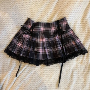 Rosa rutig minikjol - Rosa och svart rutig minikjol med knytdetalj och spets. Aldrig använd! Ungefär en storlek S