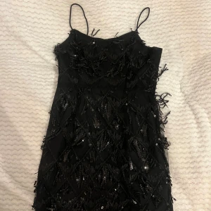 Paljett klänning - Svart klänning med paljetter, perfekt till t.ex Gatsby tema eller konsert! Slits på vänster sida. Förra ägaren klippte av lappen så osäker på storlek, men passar mig med XS-S bra!
