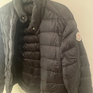 Svart dunjacka från Moncler - En svart dunjacka från Moncler med märkets logotyp på ärmen. Jackan är storlek m kvitto finns
