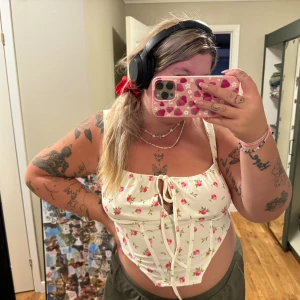 Vit blommig korsett från Shein - En vit korsett från Shein med ett blommigt mönster i rosa och grönt. Korsetten har smala axelband och en knytning framtill. Den är i storlek 1XL och har en dragkedja på baksidan. Stretchig. Endast provad.