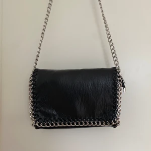 Tiamo väska  - Jag säljer min svarta Tiamo pricilla väska i storlek M då den inte kommer till användning längre. Väskan är använd men är i ett fint skick utan slitage. Längd 28cm, höjd 18cm, bred 5 cm. Jag köpte den för 550kr men säljer för 300kr!