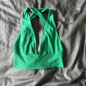 Grön ribbad halterneck topp - En grön ribbad halterneck topp med djup urringning och korsade band i nacken. Toppen är ärmlös och har en tight passform.