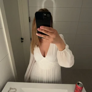 Vit klänning med långa ärmar - En elegant vit klänning med långa ärmar och v-ringad hals. Klänningen har en åtsittande midja och en plisserad kjol som ger en luftig känsla. Materialet ser ut att vara lätt och flödande, vilket gör den perfekt för både formella och semi-formella tillfällen. *Skrivet av AI, men skulle faktist vilja hålla med. Använd en gång, och det var under min guddotters namngivning. Nypris 879:- från bubbelroom. Fler bilder finns att få, hör av dig vid intresse🤠😍