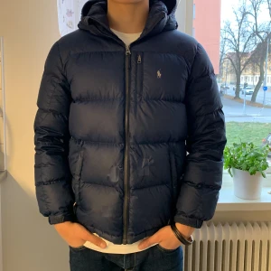 Polo Ralph lauren jacka  - Polo Ralph lauren jacka. Denna jacka passar ej mig och jag tyvärr 🥲3 hål i sig. Men har tejpats fast med blå tejp som smälter in med jackans färg. Därför ligger priset lågt på denna. Annars är den bra till vintern. Mvh Alex 