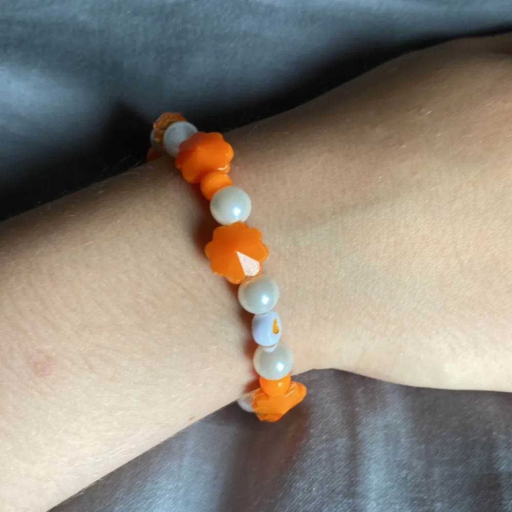 Ett orange armband med några vita pärlor på🧡🤍. Accessoarer.