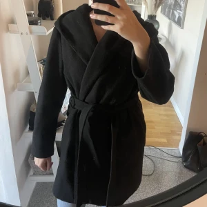Kappa från Zara - Svart kappa från Zara med knytskärp och luva. Blivit nopprig men går att få bort.
