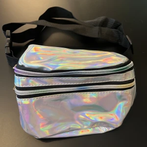 Holografisk midjeväska - Holografisk midjeväska köpt i somras. två fack fram och ett baktill mot magen.  Noterering: Något har missfärgat delar av ovansidan samt spännet förstår jag inte hur det går att spänna men det kan säkert någon av er plickare 🙆🏼‍♀️