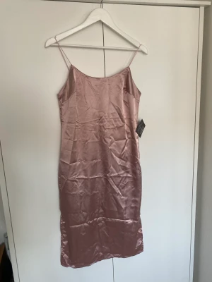 Klänning - Satinklänning i mauve/rosa från Nelly. Slits på båda sidor av klänningen. Aldrig använd men behöver steamas. 