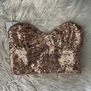 Topp - Hej!! Säljer min fina tub topp med paljetter då den aldrig kommit till användning, lapparna sitter kvar! Det är gummi längst kanten så den inte kan glida av och dragkedja på sidan! Färgen är koppar/rosa/biege typ! Sjukt fin😍