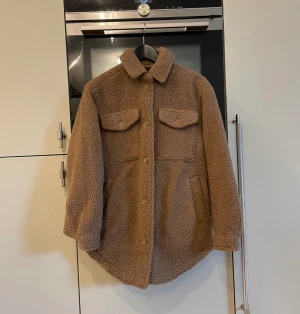 Oanvänd Teddy höstjacka, xs - Fin over size Teddy jacka i storlek XS som passar perfekt nu till hösten. Jackan är oanvänd och har sin tag kvar.   Jackan har knappar som går att knäppa upp till kragen. 4st rymliga fickor varav två med knappar vid bröstet. 
