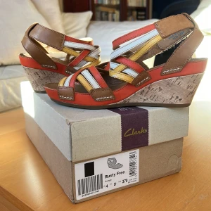 Sandaler  - Snygga, multifärgade sandaler med remmar och kilklack, av märket Clarks. Inköpta i London, använda 1 gång. Nyskick. Strlk UK4, alltså 37. Pris 200:-
