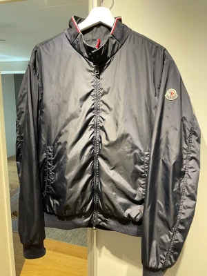Moncler jacka - Säljer min moncler vindjacka då den inte kommer nå mer till användning.  Jackan är i väldigt bra skick och knappt använd. Den är i storlek 5 sitter som en L. Skriv om du undrar över något!
