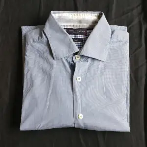 Skjorta från Tommy Hilfiger i bra skick. Ljusblå med smårutigt mönster. Bra finskjorta eller jobbskjorta. Köparen står för frakt.