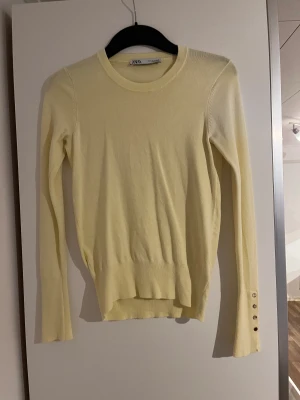 Zara tröja  - Stickad tröja från zara i pastellgul med guldknappar på ärmarna fint skick 