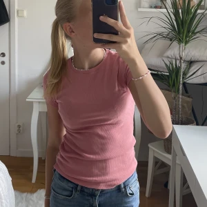 Stickad t-shirt  - Rosa ribbad t-shirt, knappt kommit till användning därför säljer jag den nu. Den är i barnstorlek men skulle säga att det är en S men passar xs och m också 