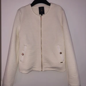 Kofta - -En kofta i mjukt material i krämvit färg med guldiga detaljer.  -Jag köpte den för 799kr -Aldrig använd -Storlek: S - 36/38