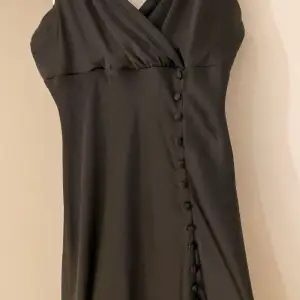 Super snygg figursydd svart klänning med V-ringning o fina knapp detaljer. Klänningen är i skönt silkestyg o i bra skick. Perfekt till nyår o jul