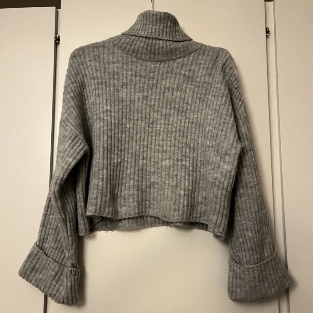 En stickad tröja från Gina tricot o en ljusgrå färg med polo krage, lite cropped i modellen  . Stickat.
