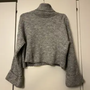 En stickad tröja från Gina tricot o en ljusgrå färg med polo krage, lite cropped i modellen  