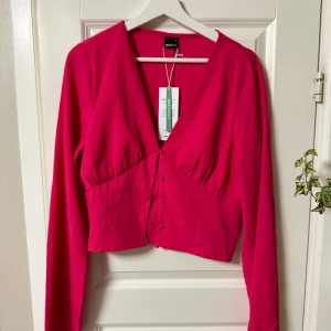 Fest tröja - Chockrosa croptop med trumpetärm, chmock i ryggen. Använd en gång, prislappen sitter kvar.