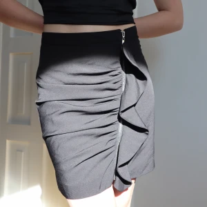 Svart kjol med volang & dragkedja - Svart högmidjad kjol från BikBok. Perfekt skick! Har en silver dragkedja placerad på framsidan med e volang till. Säljer för jag inte använder den längre 🧚🏼‍♀️