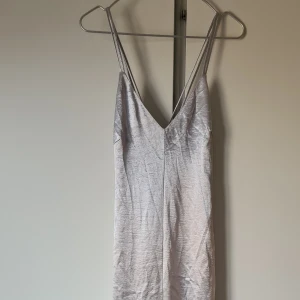 Oanvänd silvrig långklänning från h&m - Korsade band i ryggen. Oanvänd strl 38, perfekt till sommarens finfest eller bröllop
