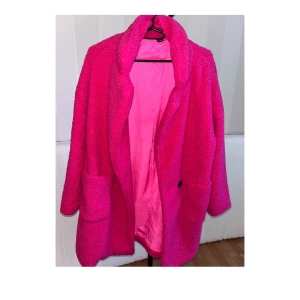 Rosa Kappa  - Oanvänt. Färg skrikrosa  Typ: Teddy  Detaljer: ficka, knappor  Fabrik: lätt strech  Material: bomullsfianell, 100% polyester