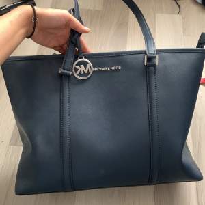 Michael Kors (äkta) Sady leather handbag används få gånger, inget fel på lädret, fin navy blue färg. Bra förvaring där man kan få plats med dator. Silver loga, längd ca 29cm, bred ca 45cm, djup 15 cm, skriv för mer bilder eller diskutera pris