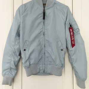 Alpha Industries bomberjacka MA-1 TT - Ljusblå bomberjacka i modellen MA-1 TT.  Något smutsig på muddar. I övrigt mycket fint skick! Nypris 1695 kr.