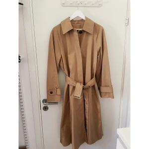 Trenchcoat från Cos storlek 38 - Använt ett fåtal gånger, så nästan nyskick. Mycket fin trenchcoat med välgjorda detaljer. 100% bomull. Delvis fodrad, innerficka. Inköpt hösten 2022 för 1750kr. Finns i butik nu. 