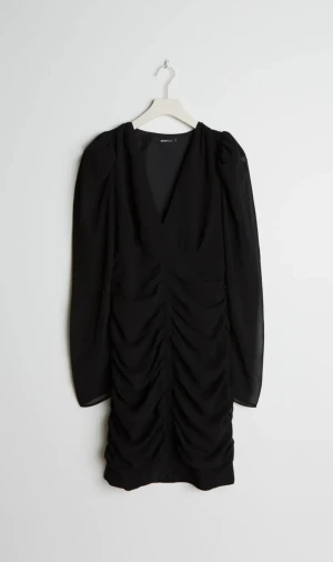 Klänning Svart - Ginatricot Stl.44 - Har en rynkning ner längs framsidan. Gjord av chiffon. V-ringad.  Aldrig använd. Storlekslapp bortklippt. Jättefin men blir tyvärr för kort på mig.  Nypris 499:-