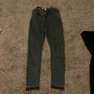 Grå/svarta jeans - Det är gråa jeans. Jeansen är från River island och är bra kvalite. Dom är straight, inte utsvängda på botten. Det står inte exakta storleken men det står 11 yrs. 