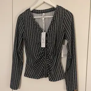 Oanvänd blus/skjorta i svart/vitt-mönster och lite rynk vid bröstet 
