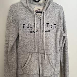 Hollister zip hoodie, ljusgrå med svart text. Sparsamt använd.