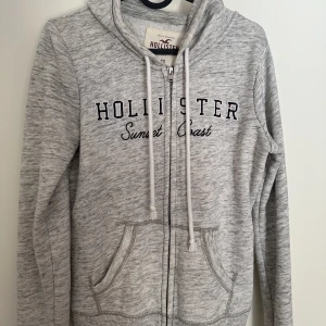 Hollister zip hoodie - Hollister zip hoodie, ljusgrå med svart text. Sparsamt använd.