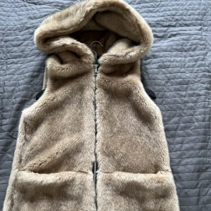 Pälsväst - Knappt använd. Jättestor luva och stora fickor. Väldigt len, skön och varm. Fuskpäls (vegansk). Passar stl xs-m.