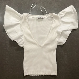 Söt Zara-topp - Storlek: S Säljer en söt, vit, ärmlös, ribbad Zara-topp med volanger och v-ringning. Knappt använd och i väldigt bra skick!💞 Hör gärna av dig vid ev funderingar💞