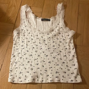 Brandy melville top i vit med blåa blommor - Vita detaljer på utlinjerna av toppen och blåa blommor på trycket 