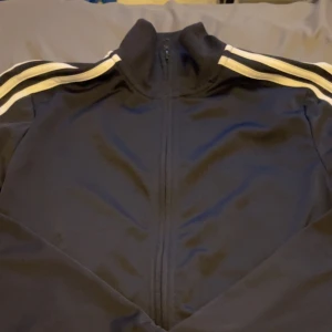 Adidas  - Kofta från adidas i storlek 164. Aldrig kommit till användning, nyskick 10/10. Svart med 3 vita ränder. 