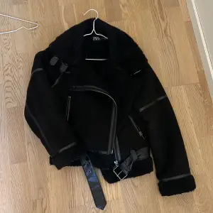 En mocka jacka från Zara i svart med skinndetaljer pp jackan. Den har två fickor fram till och är en gaska kort modell men passformen är medelstor.