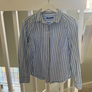 Randig skjorta  - Sommarfin skjorta, randig i vid och blå. Använd ett fåtal gånger och säljes då jag vuxit ur den. Storlek 40 från ginatricot i 100% bomull.