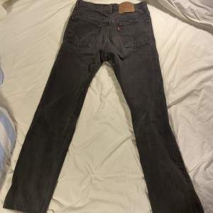 Ett par mörkgråa Levis 501 jeans i storleken W29 L30. Lägre pris eftersom det finns en del slitage i skrevet men notera att det blivit lappat och lagat. Denna modell är unisex, snygg och har hög kvalitet.