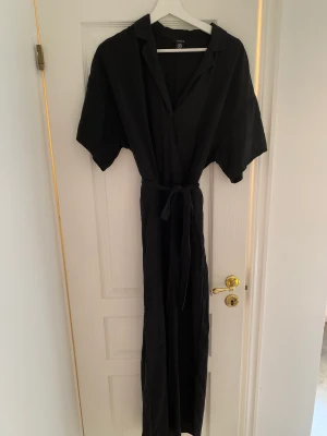 Svart Jumpsuit med vida ben - Svart jumpsuit från Lindex i storlek 44 med vida ben och ungefär som en skjortkrage! Något urringad med en ”osynlig” knapp vid brösten. Använd ungefär 2 gånger